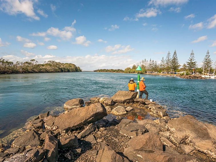 2 people fishing on the rocks at Brunswick River picnic area in Brunswick Heads Nature Reserve.