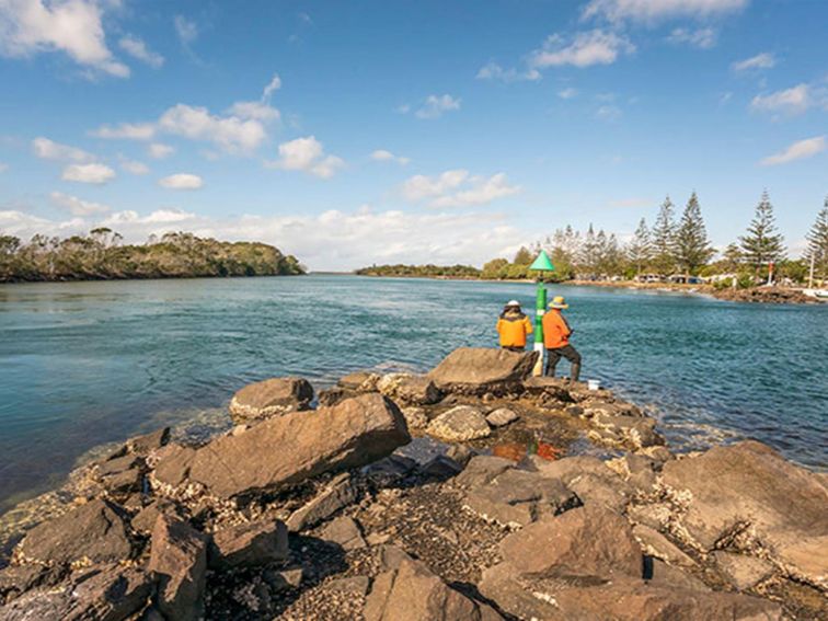 2 people fishing on the rocks at Brunswick River picnic area in Brunswick Heads Nature Reserve.