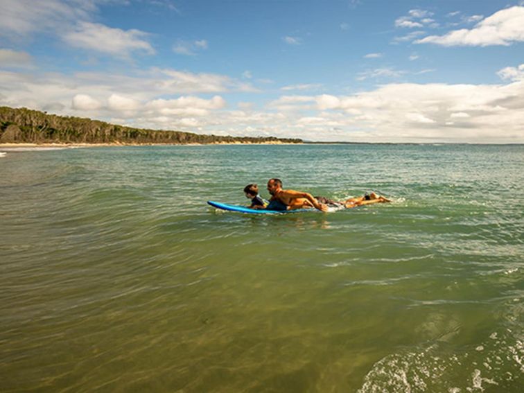 A father and young son swim on a paddle board in Bundjalung National Park. Photo: John Spencer/OEH