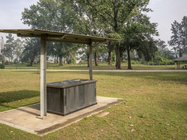 An electric barbecue underneath a shelter, with a picnic shed in the background, at Cattai Farm
