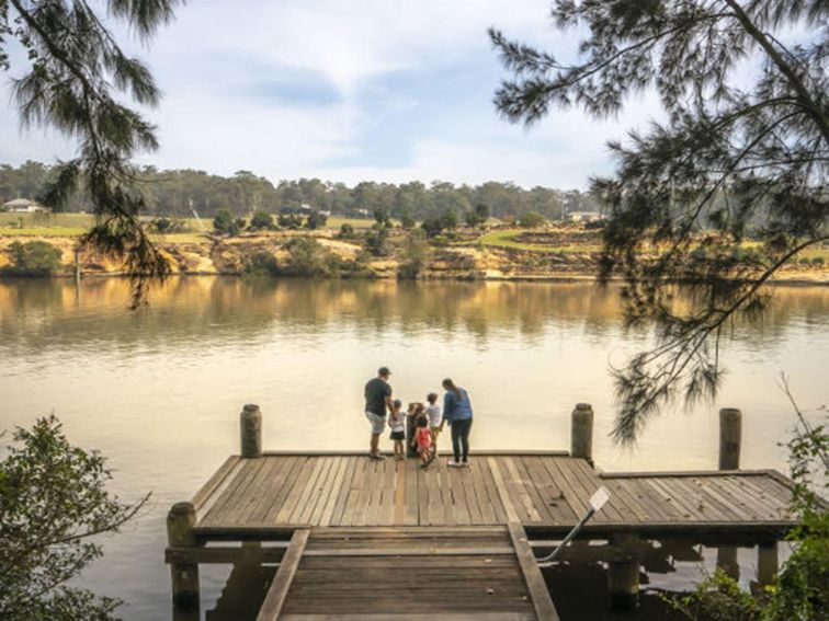 A family standing on a wooden jetty, looking across the Hawkesbury River, at Cattai Farm picnic area