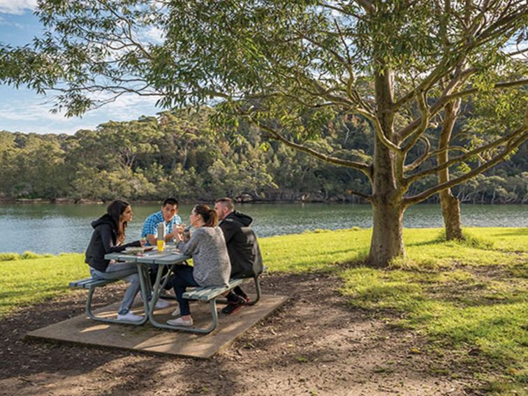 A group of friends at a picnic table next to Middle Harbour Creek in Davidson picnic area, Garigal