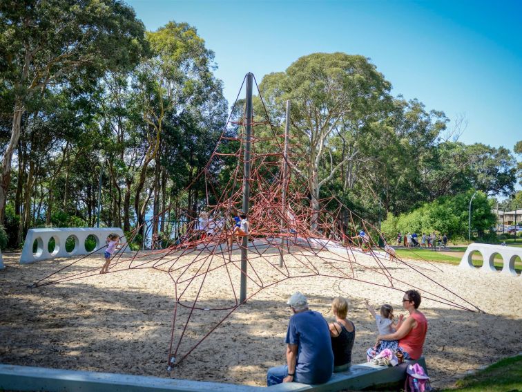 Family watching on as small children play on a large spider web playground