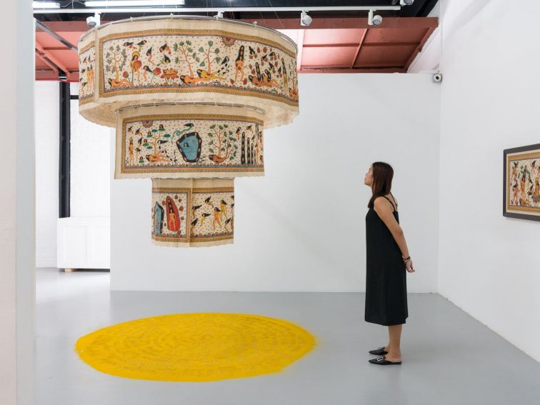 A woman stands in an art gallery viewing a circular hand painted installation