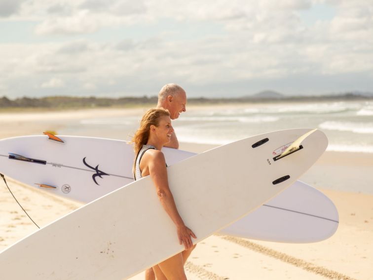 Lady and a man walking their surfboard down the beach