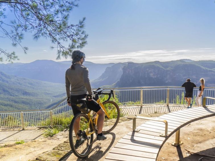A cyclist and a couple taking in the view at Evans lookout in the Blackheath area of Blue Mountains