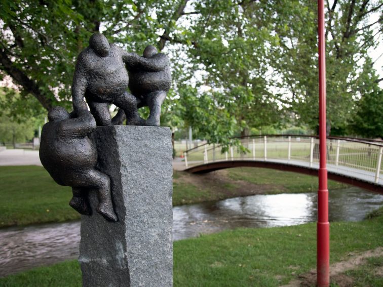 Granite sculpture with 3 figures helping each other. Situated next to a picturesque creekscape