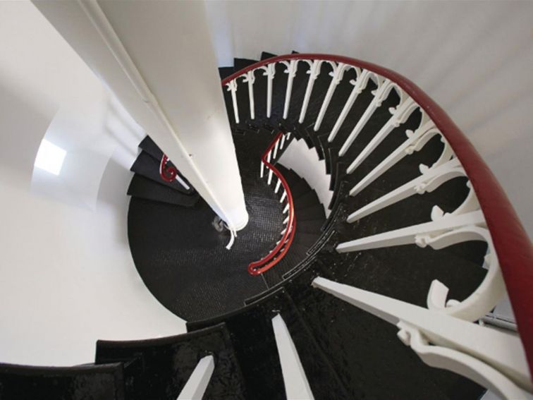 Black steel spiral staircase with white wrought iron railing and polished wood banister. Photo: Nick