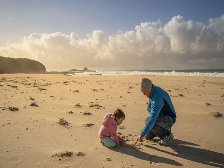 A father and baby daughter playing on the sand at the beach, Haycock Point picnic area, Beowa