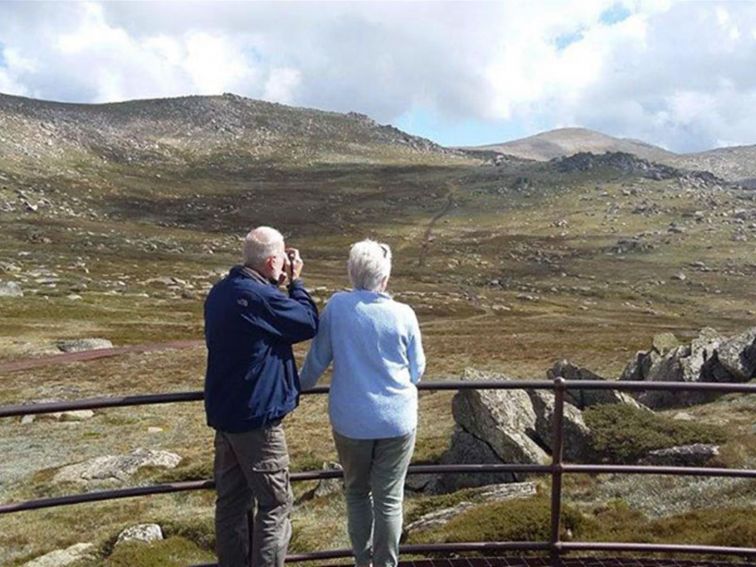 A couple take in the alpine landscape from the viewing platform of Kosciuszko lookout in Kosciuszko