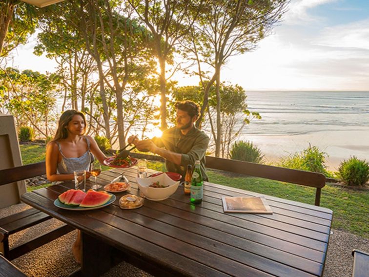 Couple eating outdoors at sunset with views of the beach from Mildenhall Cottage. Photo: John