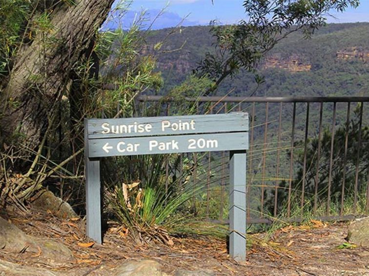 Park sign for Sunrise Point and its car park, with metal fencing and canyon vista in the background.
