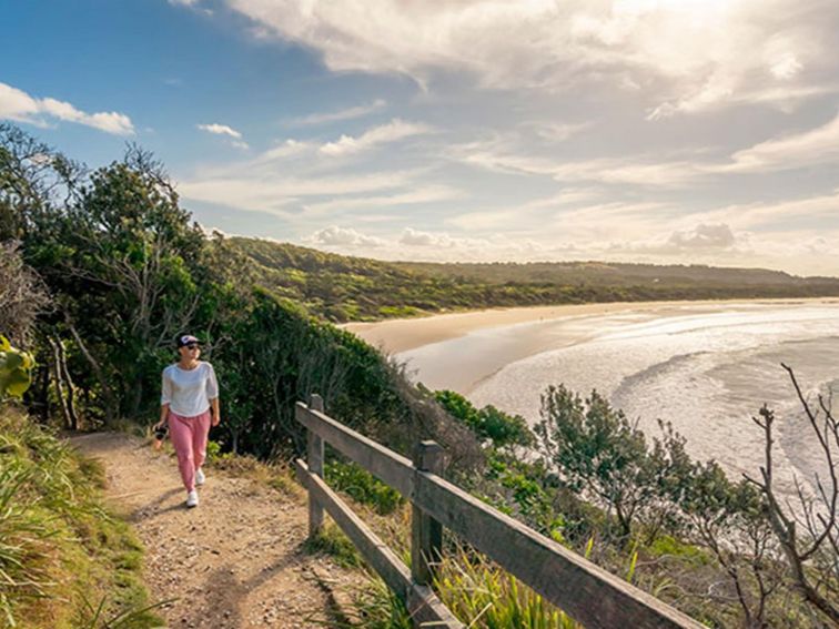 A woman walking along Three Sisters walking track, overlooking the beach in Broken Head Nature