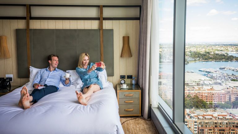Couple enjoying views of Darling Harbour from their Sofitel Sydney hotel suite (Credit: Destination NSW)