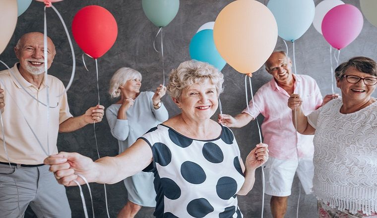 A group of mature aged men and women holding balloons and smiling