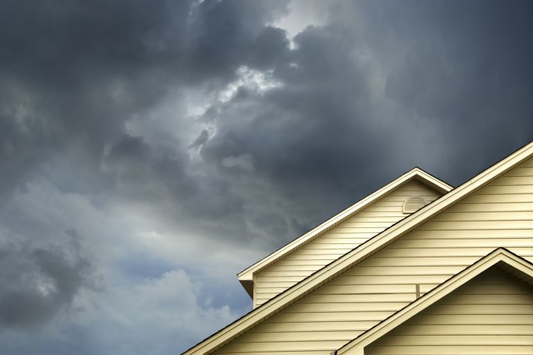 Roofline of creamy yellow weatherboard house against dark stormy sky.
