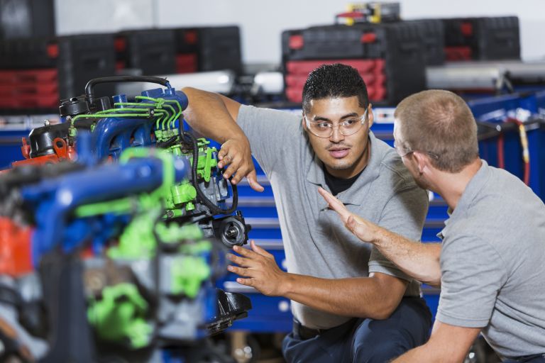 Supervisor explaining a task to an apprentice mechanic besides industrial machinery