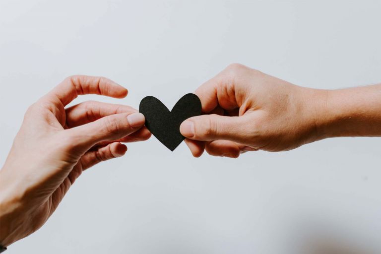 Two hands holding a black paper heart cutout