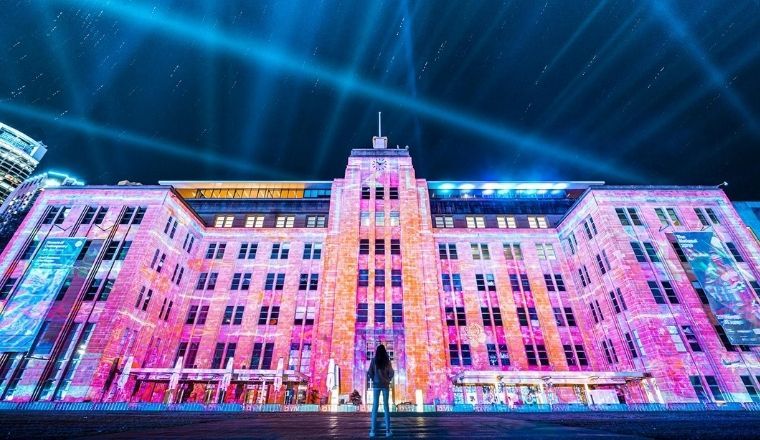 A woman stands in front of a light show projected onto the Museum of Contemporary Art at the Rocks for Vivid Sydney.