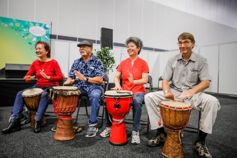 Group of seniors play happily on Djembe drums at Seniors Festival event
