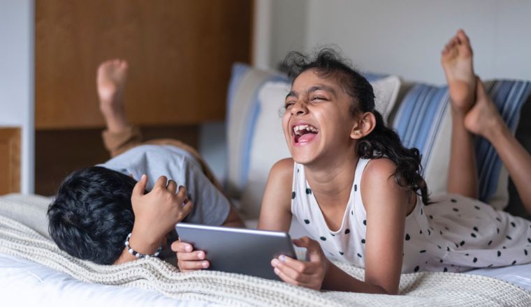 Affectionate primary school age siblings laughing while doing screen time on a tablet computer.