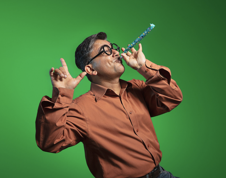 Older man in large spectacles blowing into party blower whistle