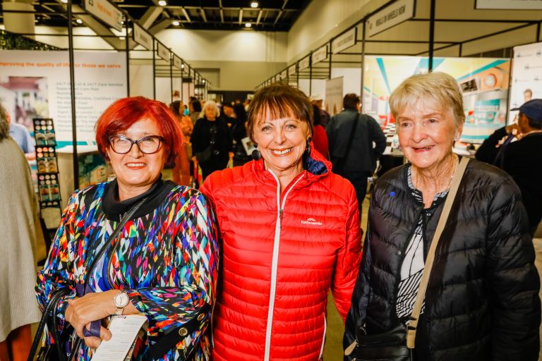 Three friends with bright hair and clothing pose and smile at the Expo