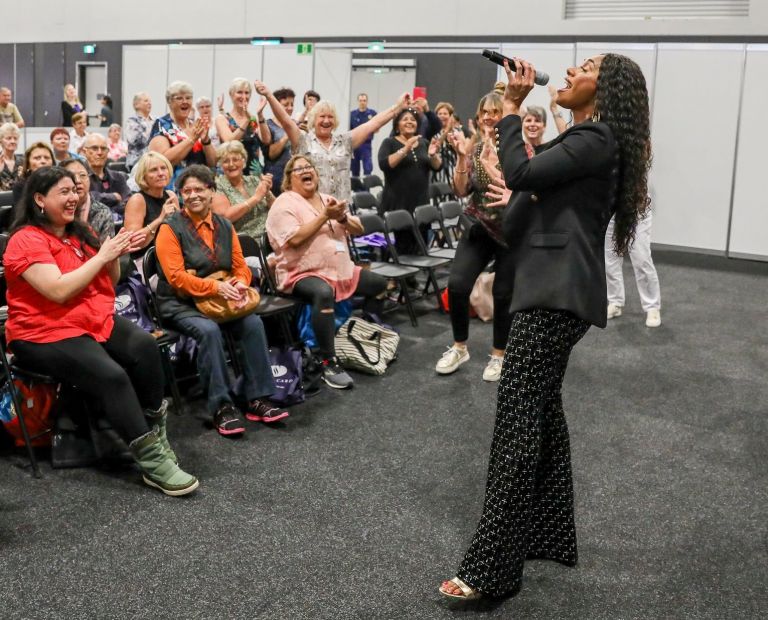 Paulini performing to excited crowd, clapping and waving their arms, at Seniors Festival Expo