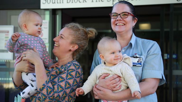 Woman and Nepean Blue Mountains Breastfeeding specialist standing outside a hospital facility holding twin babies and smiling 