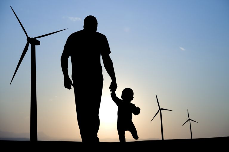 Silhouette of man and toddler strolling towards wind turbines with sun setting in background