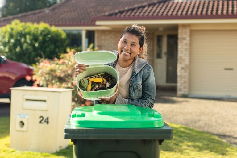 Carol, a resident of a suburban house, shows her full scrap bin next to her green bin.