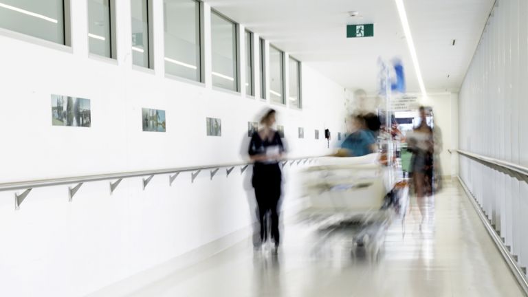 Patient being moved in a hospital bed along a corridor by two nurses and a doctor