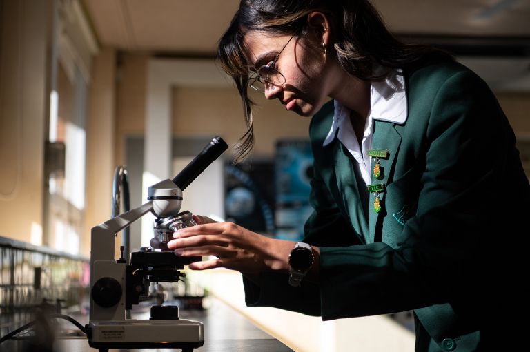 A female high school student using a microscope in a classroom