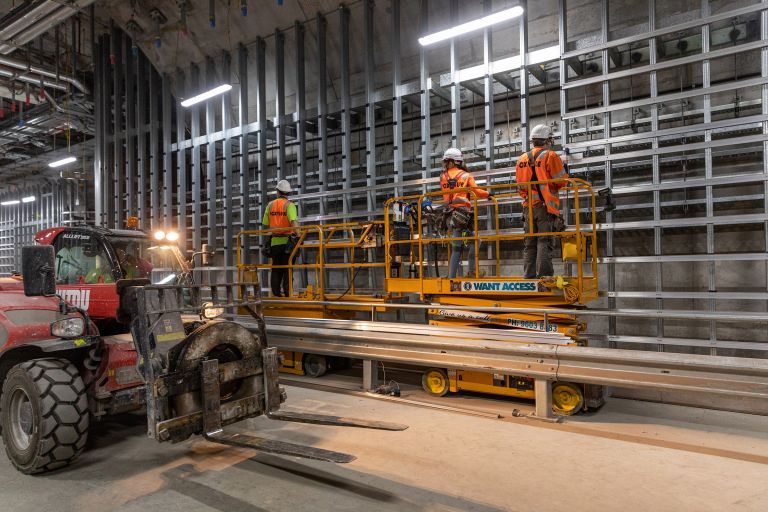 Beth working in the tunnels of the new Sydney Metro Place Station. She is with two other workers. They are all standing on a cherry picker with their back to the camera.