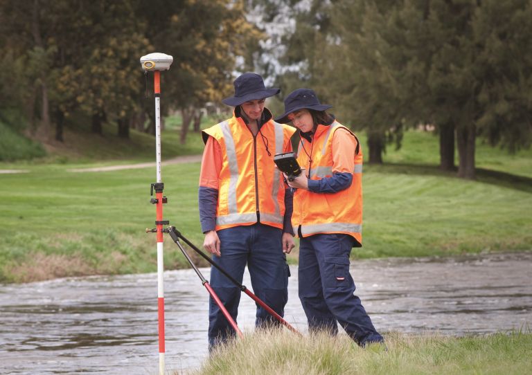 Two surveyors wearing navy bucket hats, trousers and orange vests on the Macquarie River