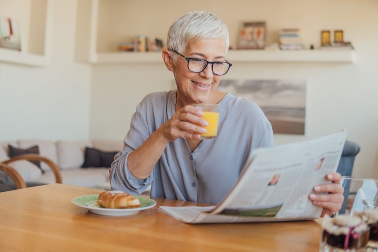 Senior woman holding newspapers while having breakfast at home