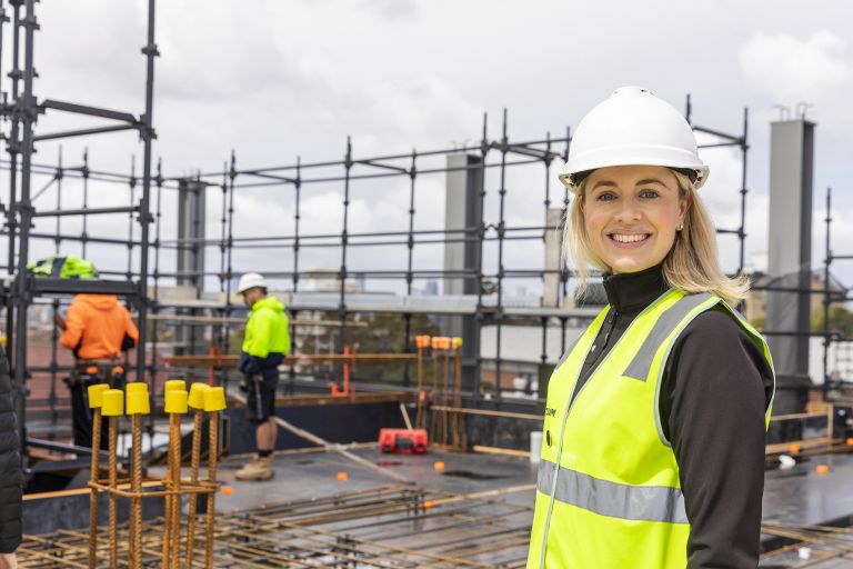Jade is standing on a construction site, smiling.