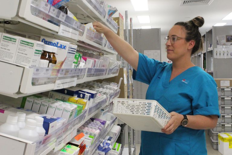 Female pharmacy worker reaching for shelf filled with boxes of medications