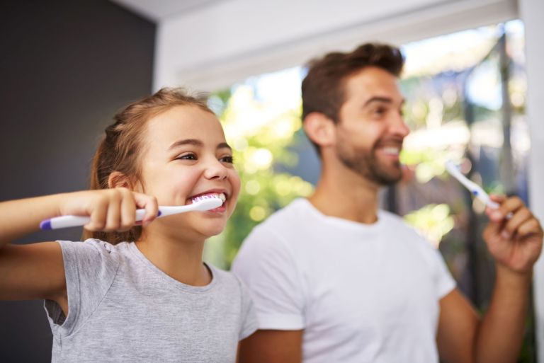 Girl and man smiling and brushing teeth