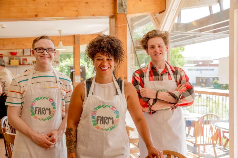 Three smiling people wearing aprons in cafe