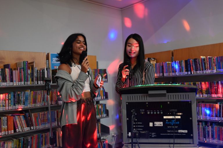 Two teenage girls singing Karaoke in the library 