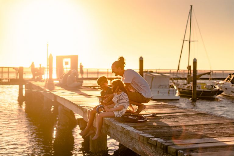 Image of woman and child fishing on a small jetty with the sun setting. 