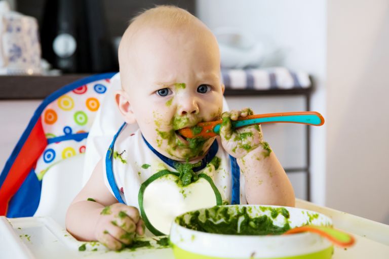 Baby in highchair eating green puree