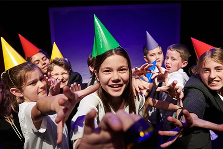Group of kids in coloured party hats laughing at camera