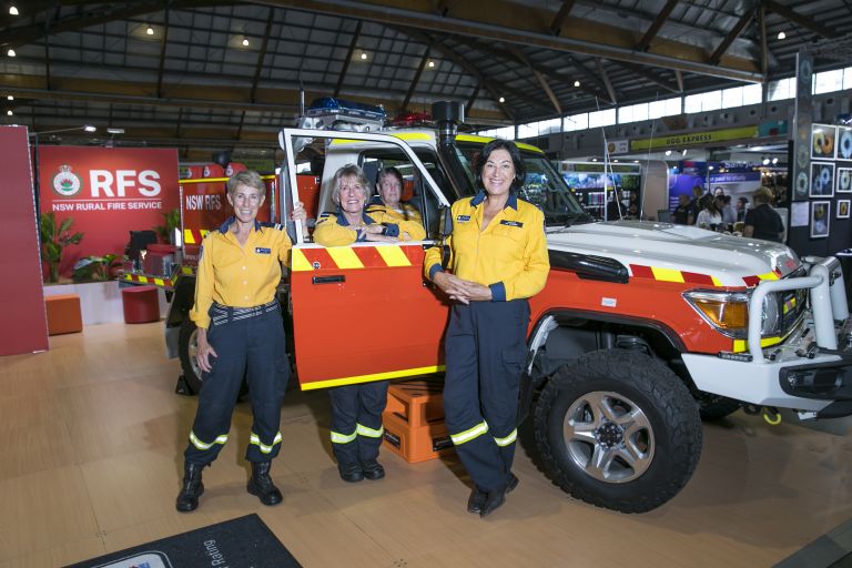 4 women wearing fire fighting ppe, standing with a small firetruck
