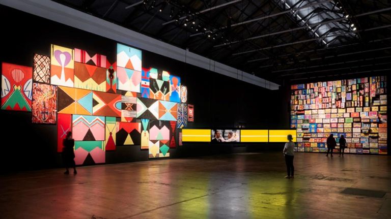 Tiny human stares up at bold artwork spotlighted on Carriageworks wall