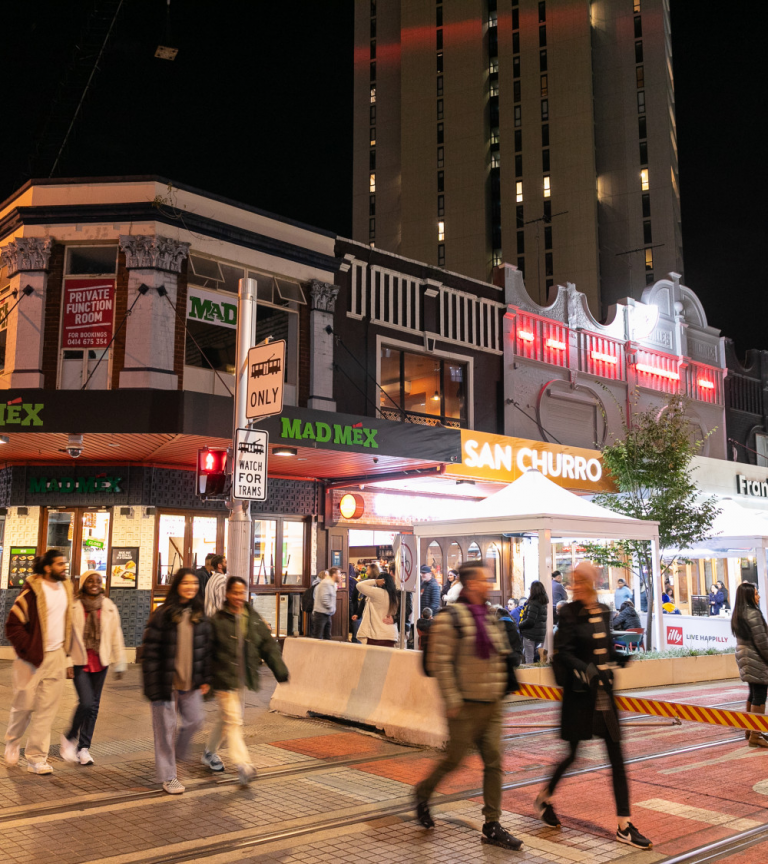 People crossing a busy Sydney street at night time.
