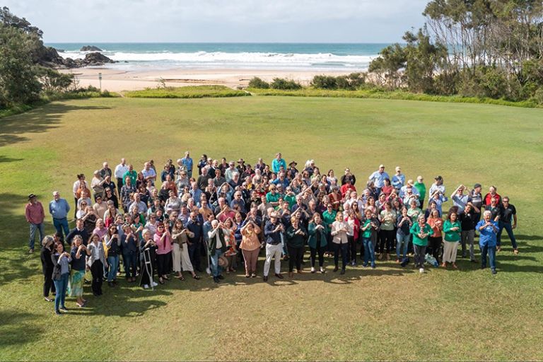 An aerial photo of a group of people in regional NSW standing on grass near a beach