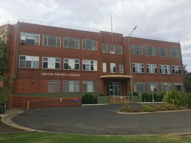 Main entrance to the Leeton Health Service building. The red brick building has a ramp access point to the left of the image and the step leading up to the main entrance to the centre-right of the image. A circular driveway is at the front of the building.