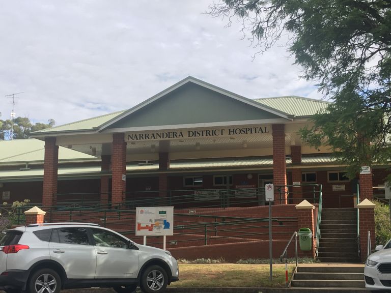 Main entrance to the Narrandera Health Service. The entrance has a ramp access to the left and steps on the right - both lead to the main entrance. A colour coded zone map of the hospital is displayed outside the main entrance. Public parking spots are shown outside as well. 